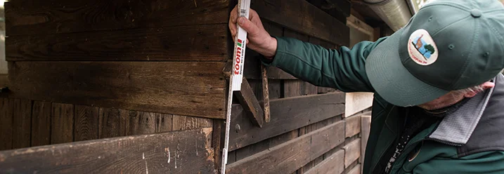 Person misst Holzbalken mit Zollstock aus